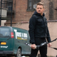 Hawkeye (Jeremy Renner) looks serious standing with his bow and arrow in hand and a green van next to him that says TRUST A BRO